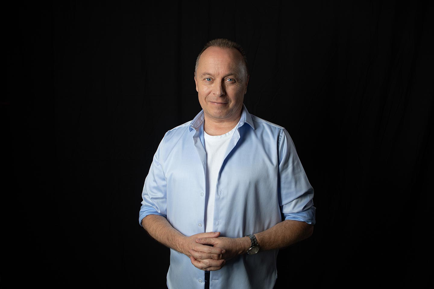 Christoph Rosenberger steht entspannt mit gefalteten Händen vor dunklem Hintergrund.