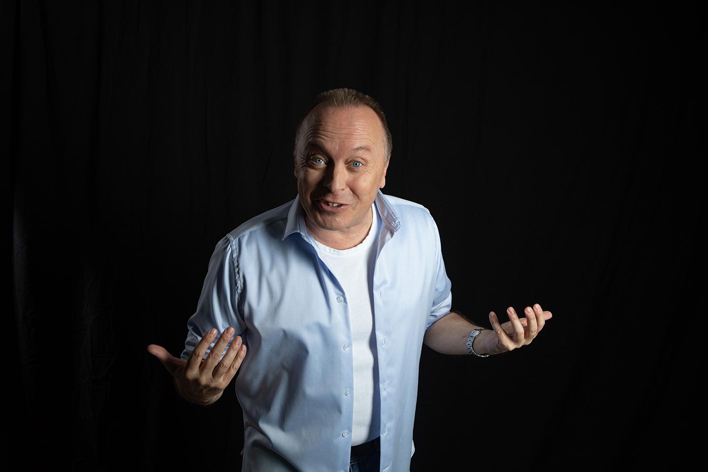 Christoph Rosenberger hält die Hände offen zur Seite und blickt fragend in die Kamera vor dunklem Hintergrund.