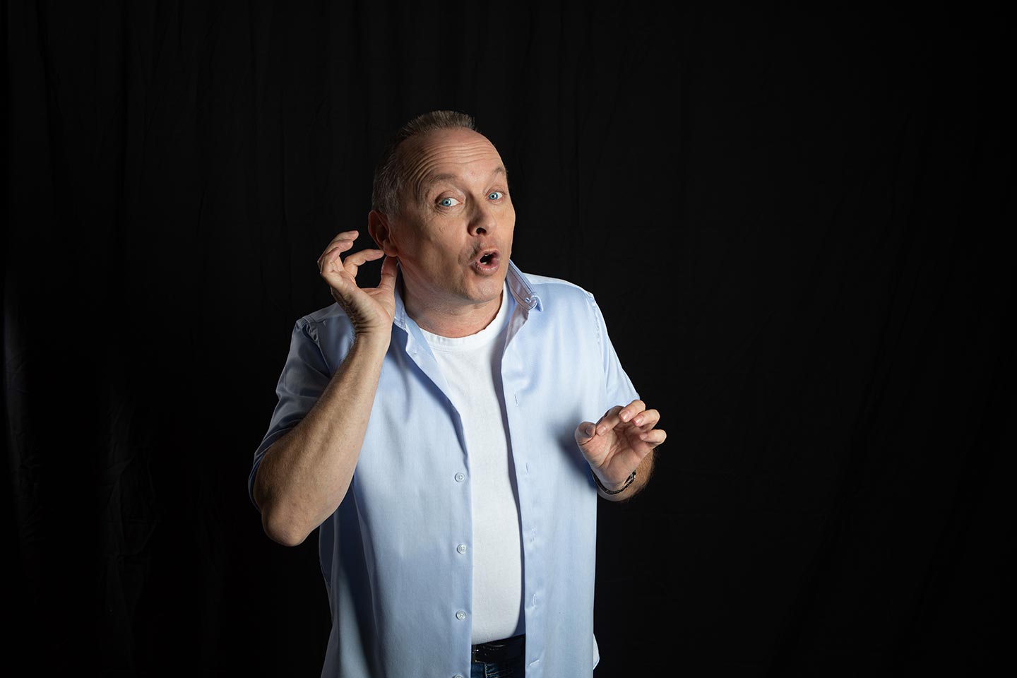 Christoph Rosenberger hält eine Hand am Ohr und blickt aufmerksam nach vorn vor dunklem Hintergrund.